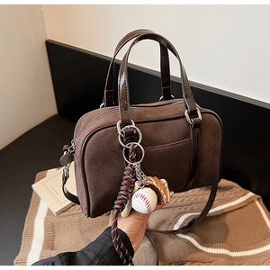 Detail view of brown suede Boston bag featuring baseball glove charm and premium leather handle