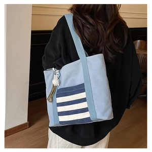 Detail of light blue canvas tote bag with striped side pocket and fluffy charm on a model