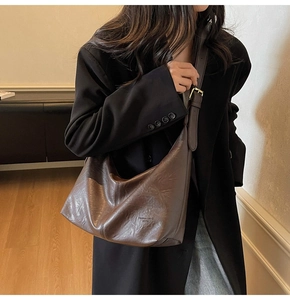 Close-up of a vintage brown leather crescent bag worn over a black winter coat