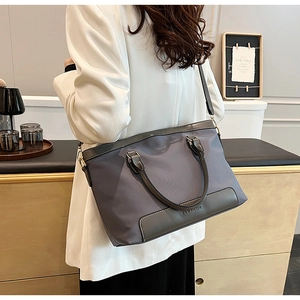 Détail d'un sac cabas en nylon avec poignées en cuir et ferrures métalliques sur tissu gris