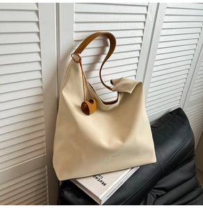 Macro shot of off-white leather tote bag with brown straps and orange heart pendant