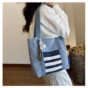 Detail view of light blue canvas tote bag with striped pocket and plush charm on strap