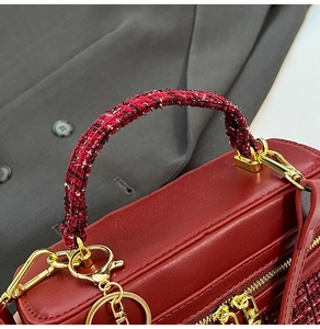 Detail of red square handbag with tweed-wrapped handle and golden hardware zippers