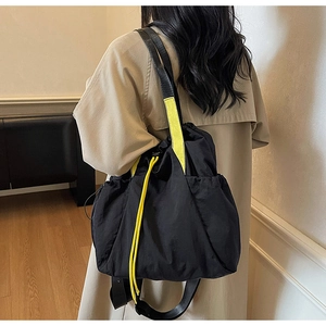 Detail of a black canvas tote with bright yellow drawstrings and wide shoulder straps