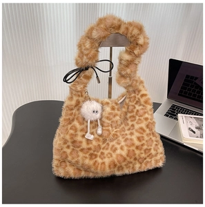 Detail view of leopard print plush handbag with fluffy monster charm on a desktop stand