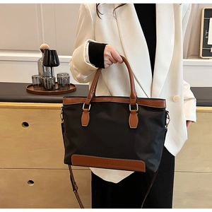 Détail du sac fourre-tout en nylon noir avec poignées en cuir marron et logo CELAROK
