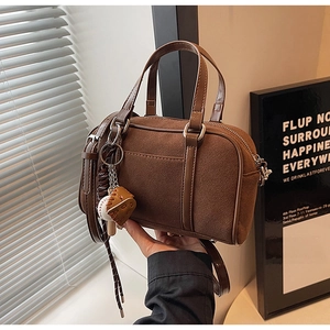 Detail of a dark brown suede Boston bag with a baseball glove charm and leather strap