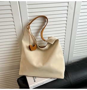 Detail view of cream tote bag with caramel leather strap and heart-shaped pendant
