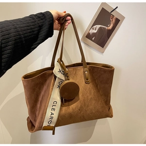 Macro shot of brown suede tote bag with decorative lettered strap and round pouch charm