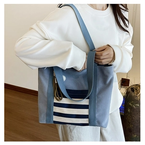 Detail view of a blue canvas tote bag featuring white horizontal stripes and blue webbing straps
