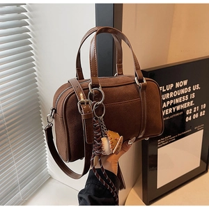Detail view of brown suede Boston bag with leather handles and baseball glove charm