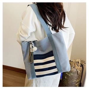 Detail of light blue canvas tote bag with striped front pocket and white pompom charm