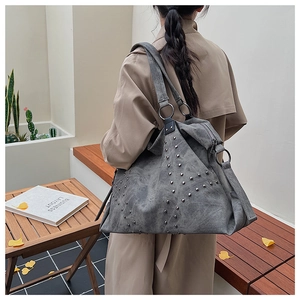 Grey tote bag with silver studs on textured faux suede shown on a model's shoulder