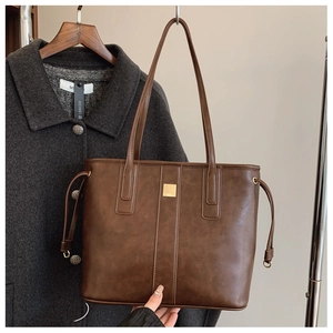 Detail of dark brown leather tote bag with vertical stripes and golden metal hardware