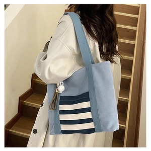 Detail view of the blue canvas tote bag with striped front pocket and fuzzy ball charm