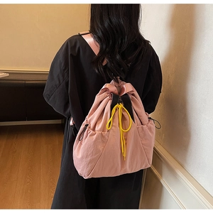 Pink nylon drawstring backpack with yellow straps worn by model in a cozy home setting