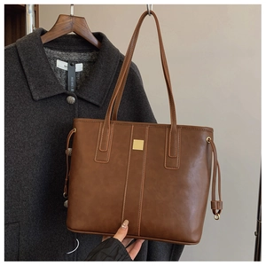 Detail of dark brown faux leather tote bag with gold metal buckle and vertical stitching