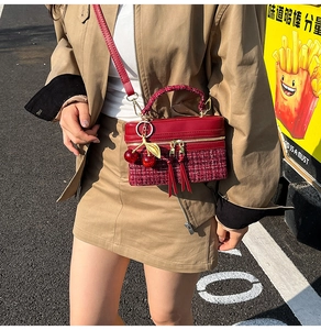 Close-up of red leather and tweed handbag with golden hardware and cherry charm