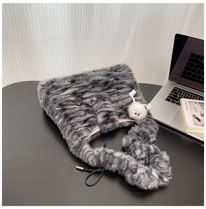 Detail of grey faux fur tote bag with plush monster charm on a modern desk setup
