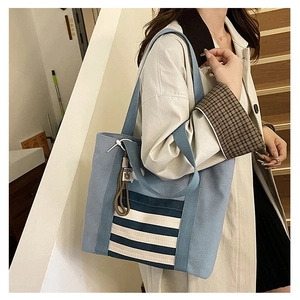 Detail of a large light blue canvas tote bag with navy stripes on a female model shoulder