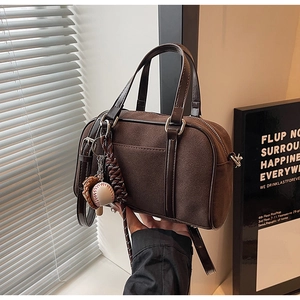 Detail of dark brown matte Boston bag with glossy handles and baseball charm
