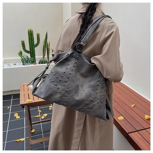 Lifestyle shot of a dark grey tote bag with vintage metal rivets on a woman's shoulder