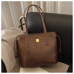 Macro detail of dark brown leather tote bag featuring a minimalist gold square metal buckle
