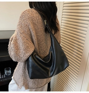 Minimalist black leather hobo bag with gold logo shown on model in home setting