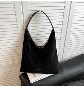 Detail of minimalist black suede hobo bag with white logo and fine stitching on a sofa