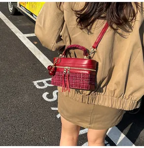 Detail of red tweed and leather handbag with cherry charm worn on camel jacket