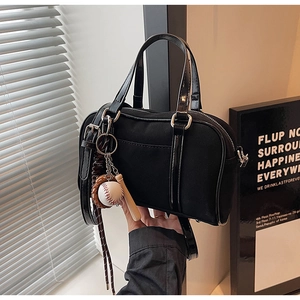 Detail of black canvas Boston bag with baseball charms and glossy leather handle