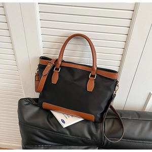 Détail du sac cabas en nylon noir avec bordure en cuir marron et logo embossé sur le côté