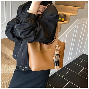 Gros plan sur un sac cabas marron avec logo doré et pendentif lapin sur une bandoulière
