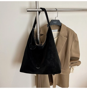 Detail of minimalist black tote bag with white stitching and brand text on matte suede