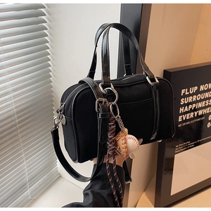 Detail view of black Boston bag with glossy handles and a baseball charm accessory