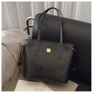 Detail of black tote bag with gold metal hardware and side drawstring on leather seat