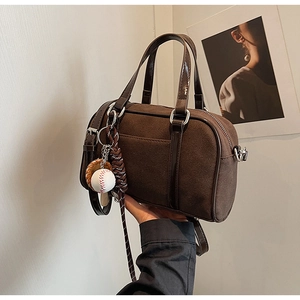 Detail of Boston bag in dark brown suede with leather handles and baseball charm accessory