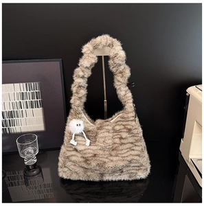 Detail of tan wavy plush shoulder bag featuring a cute white monster pendant accessory