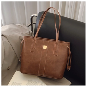 Detail of a dark brown leather tote bag with a gold square buckle in a lifestyle setting