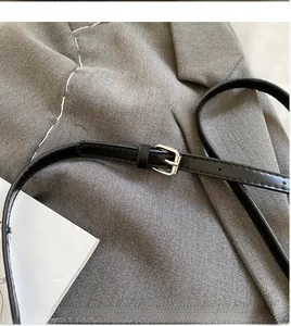 Adjustable black faux leather shoulder strap with silver buckle on a grey suit jacket