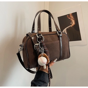 Detail of a brown suede Boston bag with leather handles and baseball glove pendant