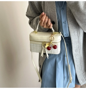 Detail of cream box bag showing mixed leather and woven texture with cherry charm