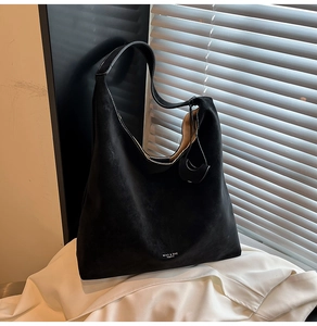 Detail of matte black suede tote bag showing widened shoulder strap and branding