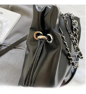 Detailed close-up of glossy black leather bucket bag with silver metal eyelets and chain strap