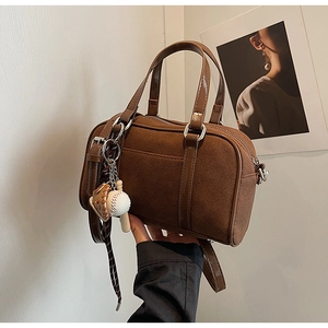 Brown suede Boston bag with baseball charm shown in a minimalist lifestyle setting
