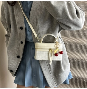 Close-up of cream white structured crossbody bag with realistic cherry charm and woven detail