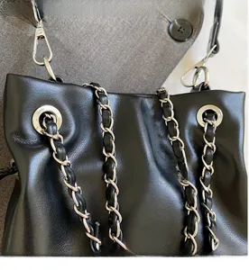 Detail of black leather bucket bag with silver metal eyelets and woven chain strap