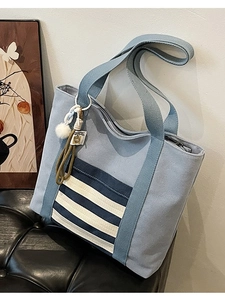 Light blue canvas tote bag with striped pocket and fluffy pendant on a black leather chair