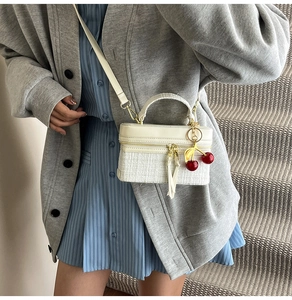 Detail of cream box bag featuring woven texture, dual zippers and red cherry charm