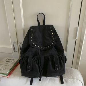 Detail view of black suede backpack featuring silver studs, flap pockets and drawstring closure